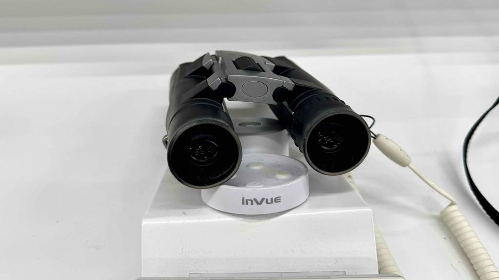 Das getestete 10 x 25-Fernglas in Schwarz liegt gesichert, mit Fokus auf die Gläser, auf einem weißen Ausstellungspodest.