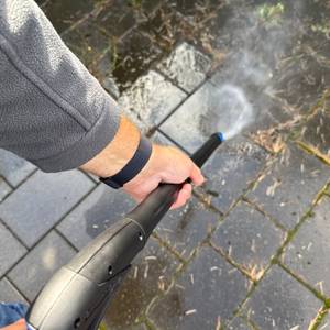 Zwei Hände reinigen einen gepflasterten Boden mit dem Nilfisk E 145.4-9 X-TRA