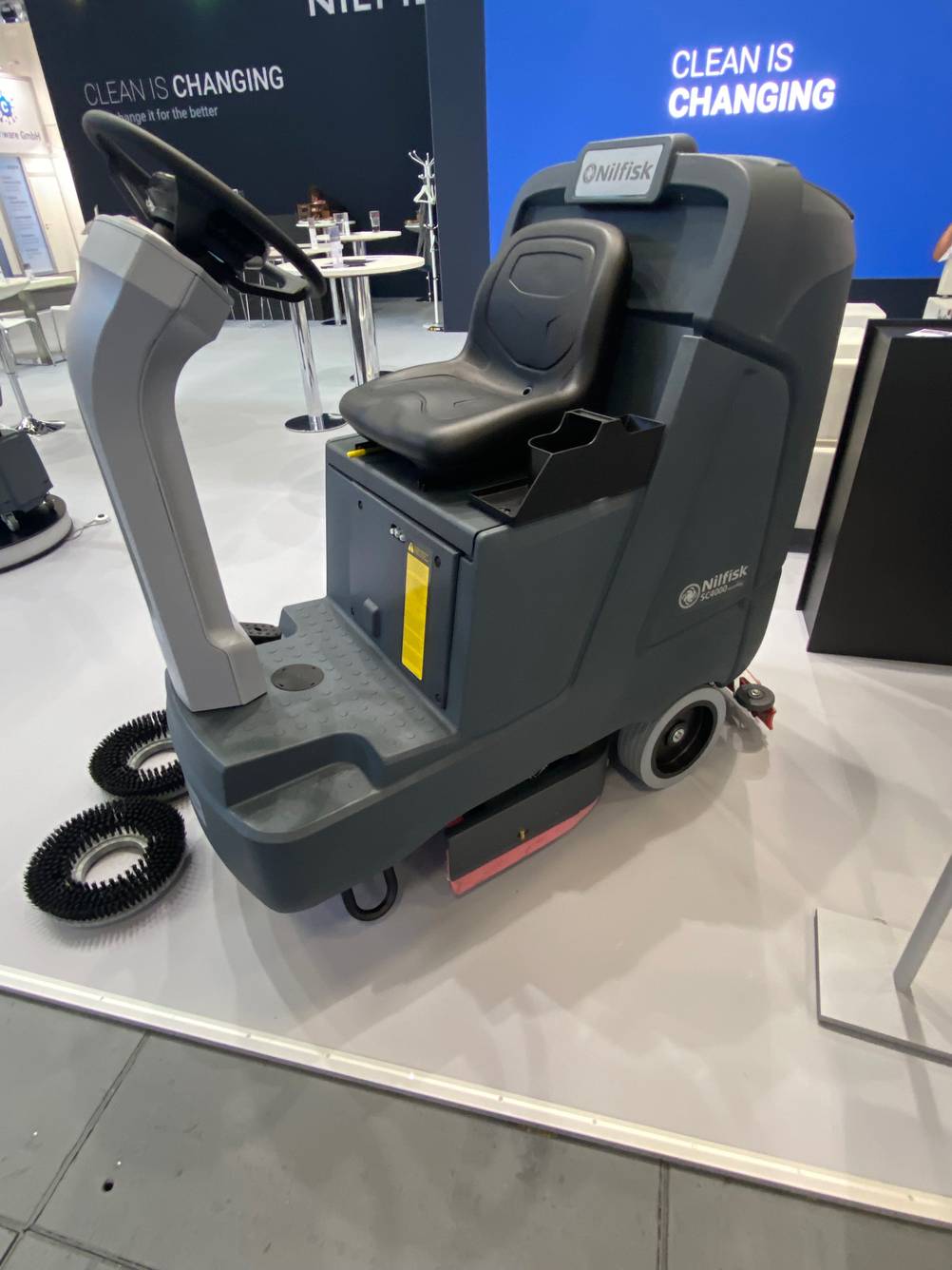 Scheuersaugmaschine im Test: ein fahrbares Modell der Marke Nilfisk inklusive Ersatzbürsten steht in einem Ausstellungsbereich.
