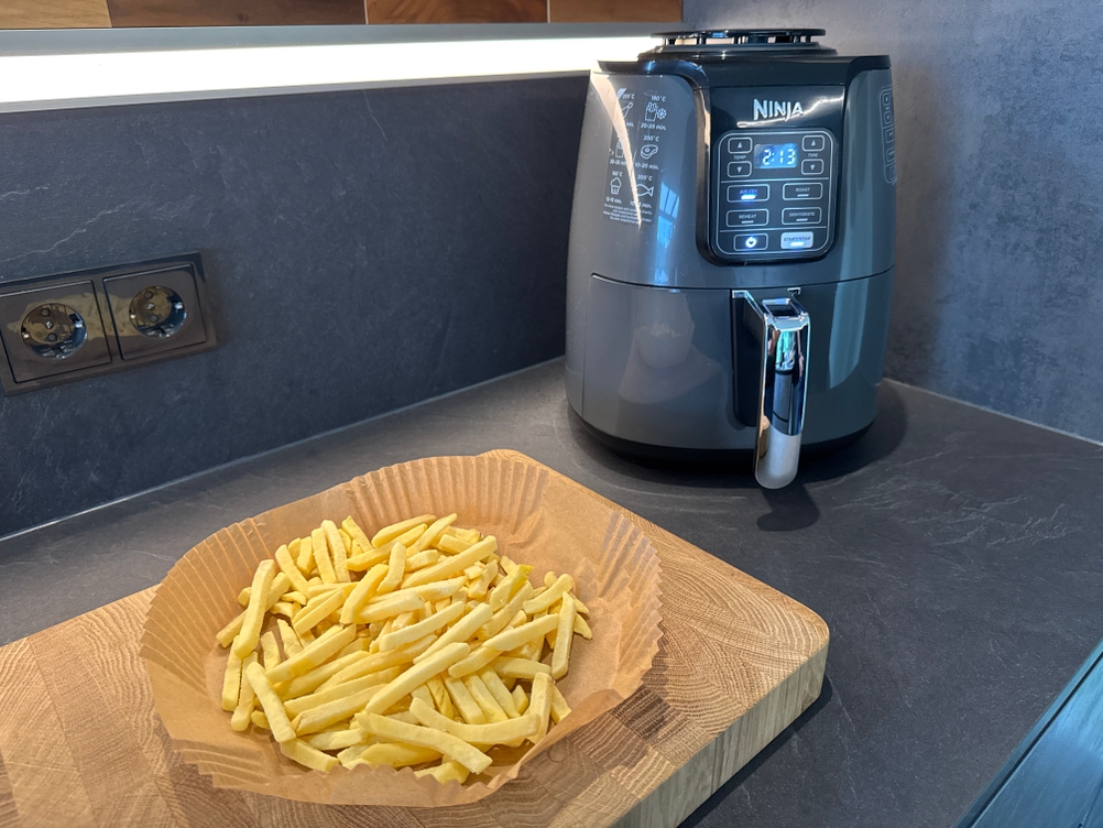 Pommes liegen in einem Backpapier vor der Ninja AF100EU.