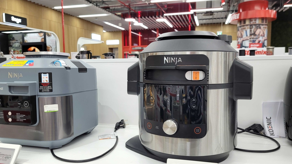 Mehrere Multikocher-Geräte stehen zum Testen nebeneinander auf einem Regalbrett.