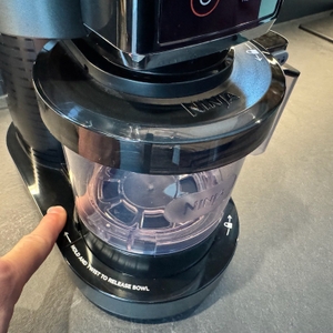 Der Knopf zur Entriegelung des Behälters der Ninja NC300EU wird von einer Hand gedrückt.