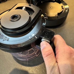 Eine Hand drückt den Knopf zur Entriegelung des Deckels der Ninja NC300EU.