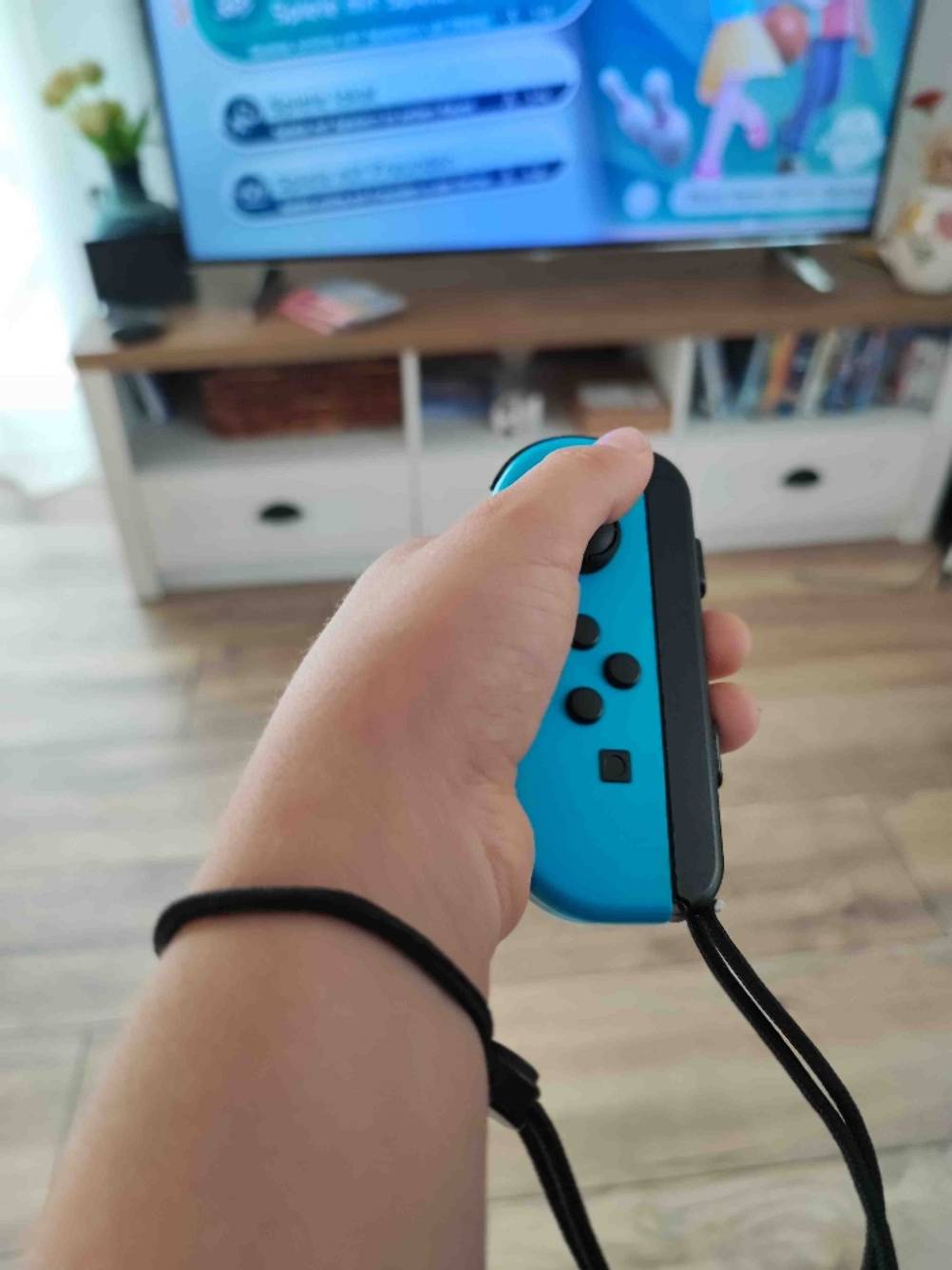 Eine Hand hält die blaue Seite eines Nintendo-Switch-Controllers auf den Bildschirm gerichtet.