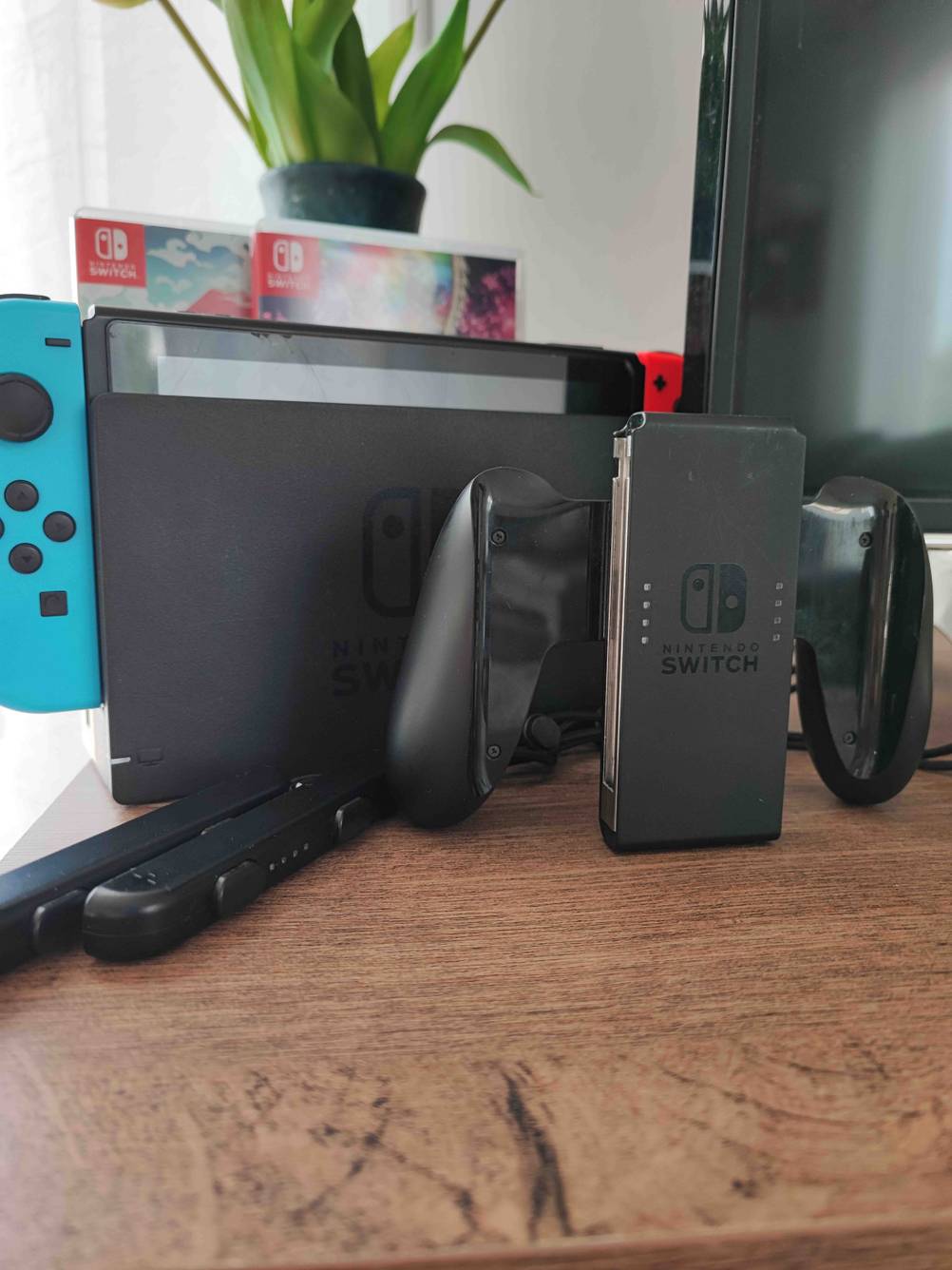 Zwei getestete Nintendo Switch Controller stecken in einer Konsole, die mit Zubehör und Spielen auf einer Holzfläche steht.