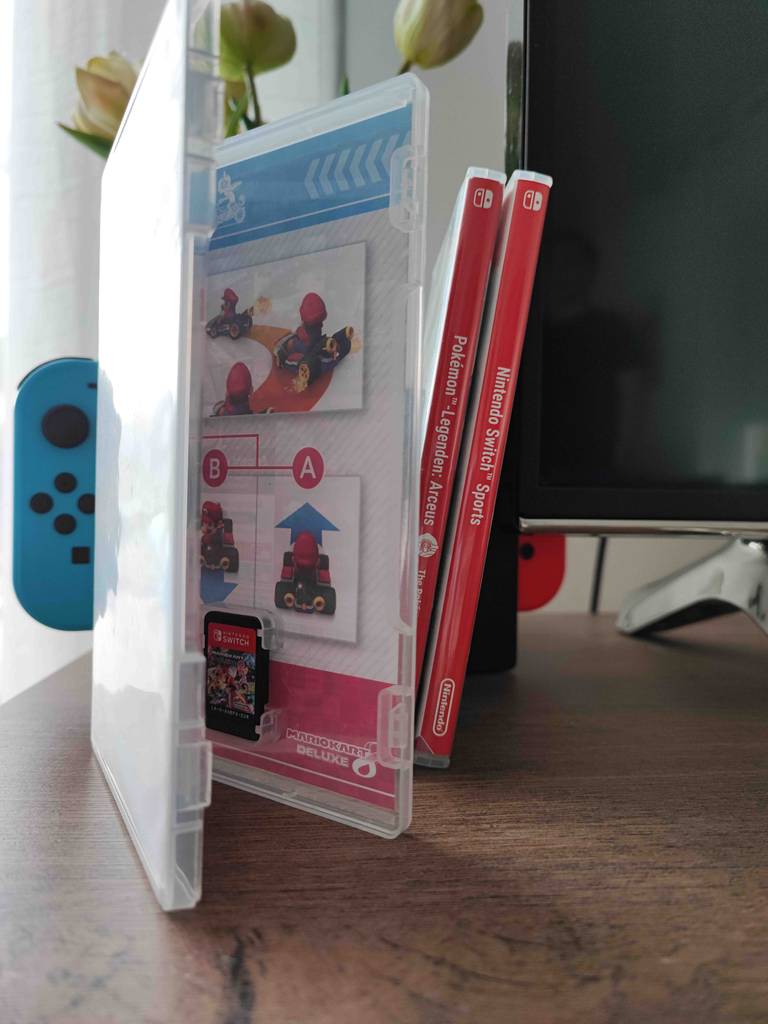 Nintendo-Switch-Spiele-Test: drei Spiele-Boxen mit Spiel-Karten neben einem Fernseher und zwei Nintendo-Switch-Controllern.