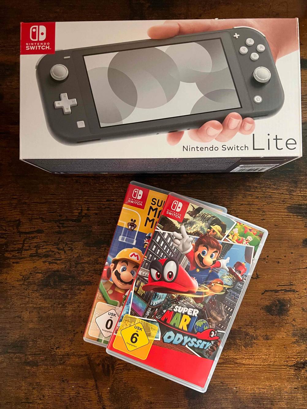 Zwei getestete Nintendo Switch Spiele liegen vor einer verpackten Konsole auf dunkler Holzfläche.