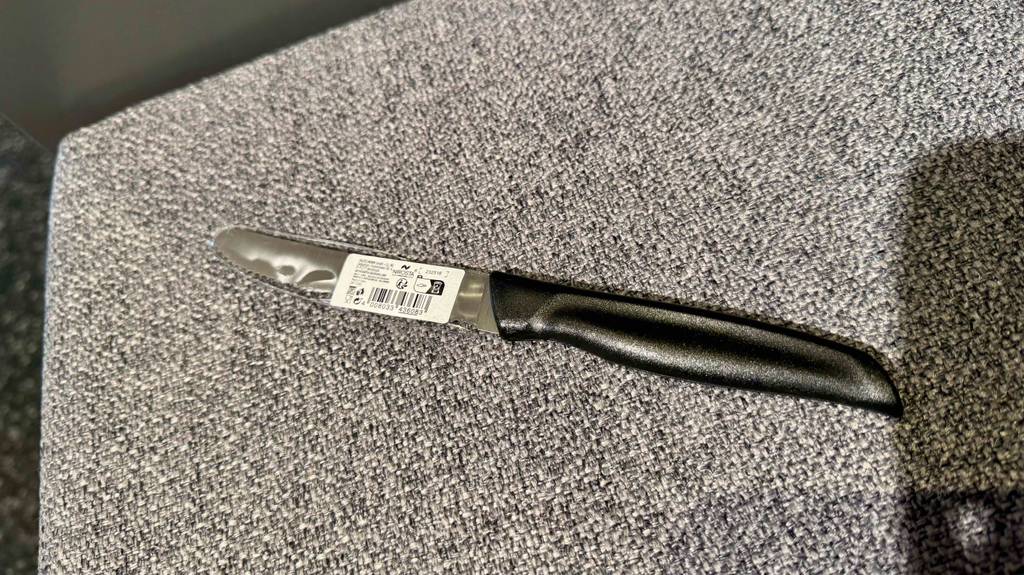 Frühstücksmesser im Test: Ein kleines Messer mit schwarzem Griff und Wellen geschliffener Klinge liegt auf einem grauen Gewebe.