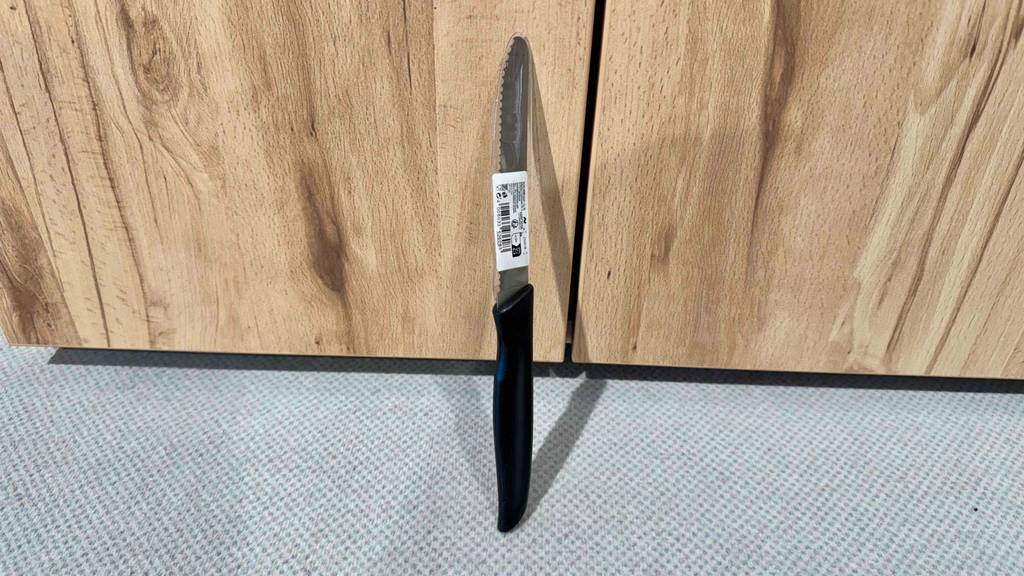 Frühstücksmesser-Test: Ein kleines Messer mit schwarzem Griff und Wellenschliff lehnt an einem Holzkasten.