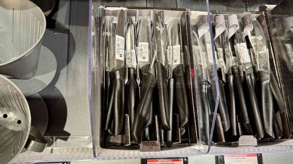 Mehrere getestete Frühstücksmesser mit schwarzen Griffen und Klingen inklusive Wellenschliff liegen auf einem Verkaufsregal über- und nebeneinander.