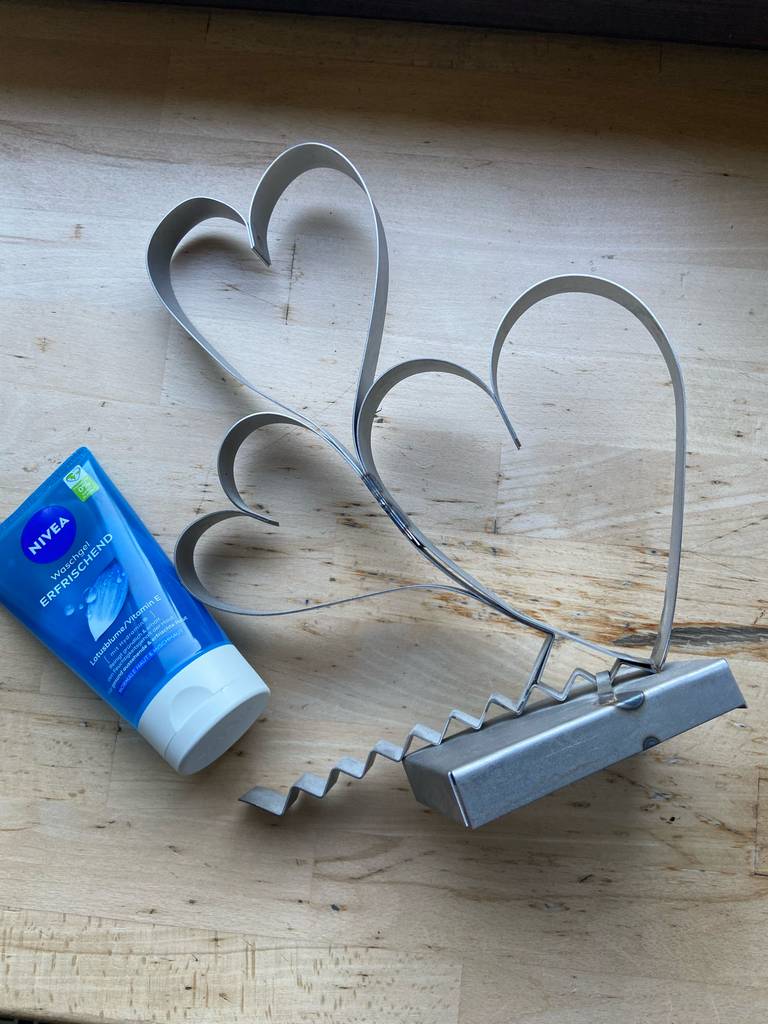 Die milde Gesichtsreinigung im Test in einer blauen NIVEA-Tube liegt neben einer Herz-Dekoration auf einer weißen Holzoberfläche.