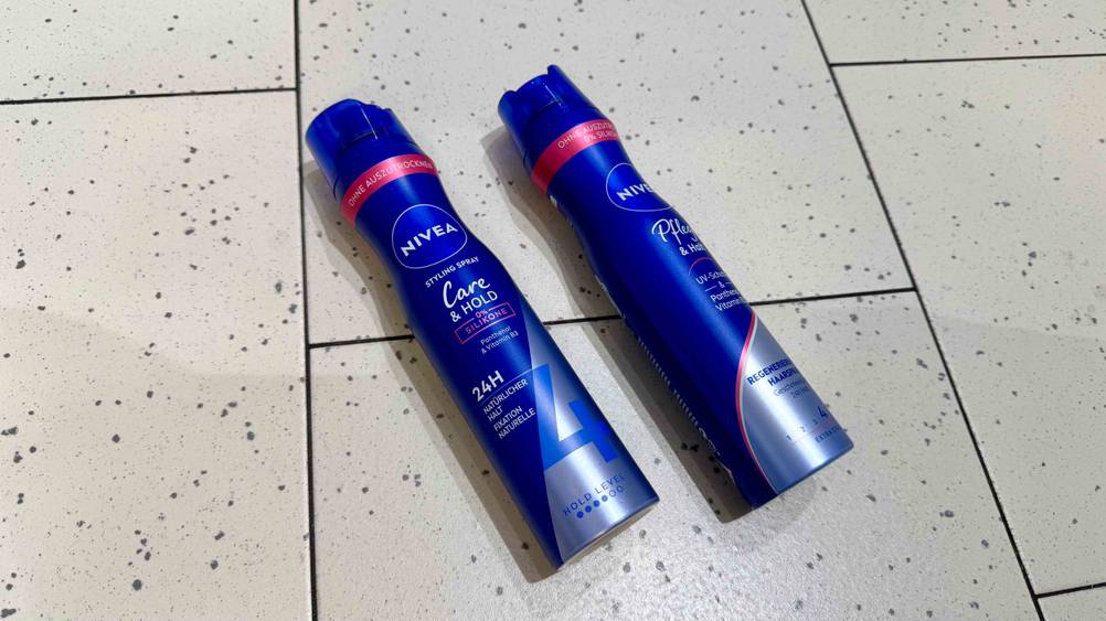 Auf einem hellen Boden liegen leicht quer zwei Dosen Nivea-Haarspray im Test nebeneinander.