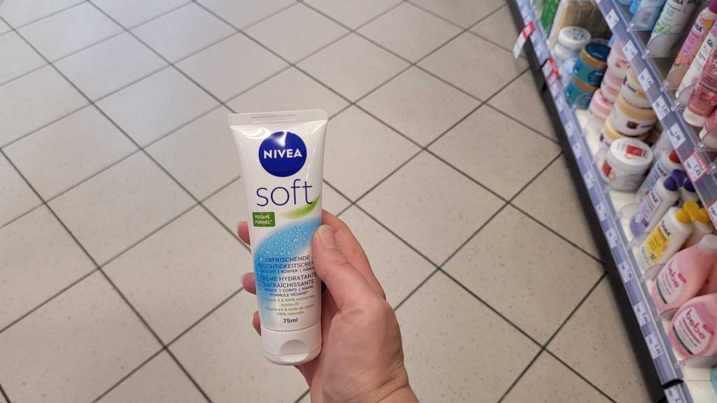Im Test: Eine Hand hält eine Tube Nivea-Gesichtscreme über einem Fliesenboden.