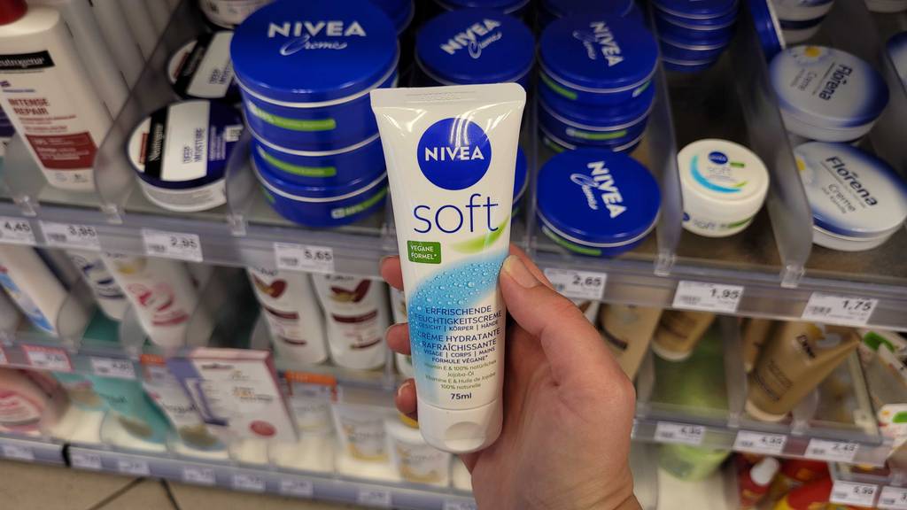 Nivea-Gesichtscreme im Test: Eine Hand hält eine Tube vor einem Kosmetikregal.