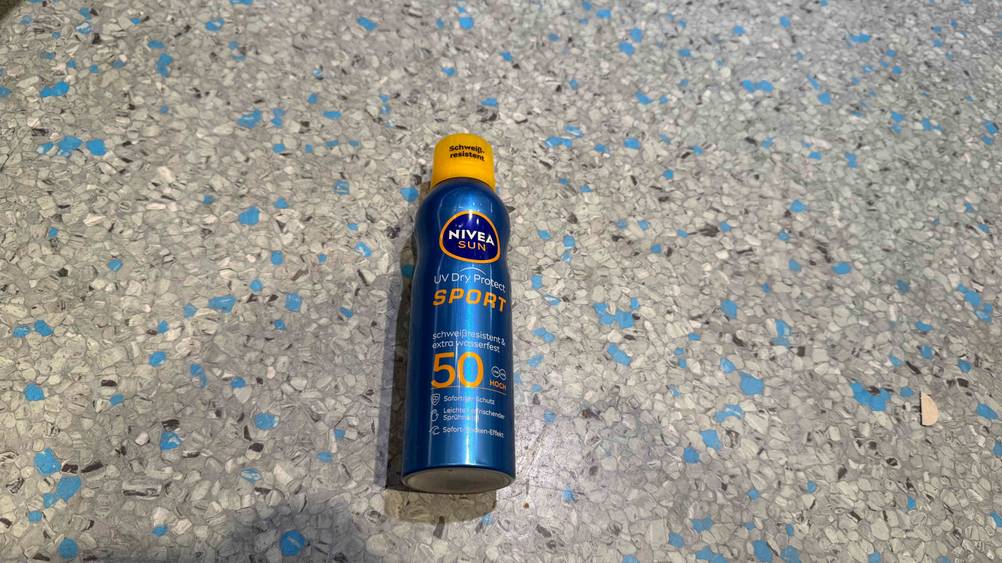Eine Flasche des Nivea-Sonnensprays im Test von oben auf einem grau-blauen Boden liegend.