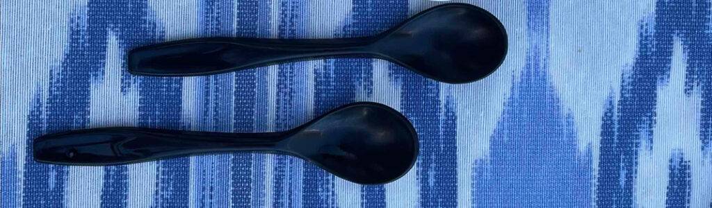 Zwei schwarze Eierlöffel im Test liegen auf einem blau-weißen Gewebe.