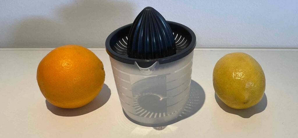 Orangenpressen-Test: Ein Modell inklusive Liter-Anzeige steht zwischen zwei Zitrusfrüchten.