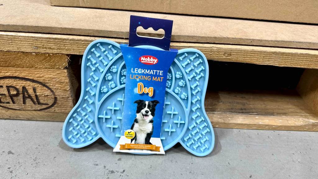 Die hellblaue Hunde-Leckmatte im Test lehnt innerhalb ihrer Verpackung an einer Holzpalette.