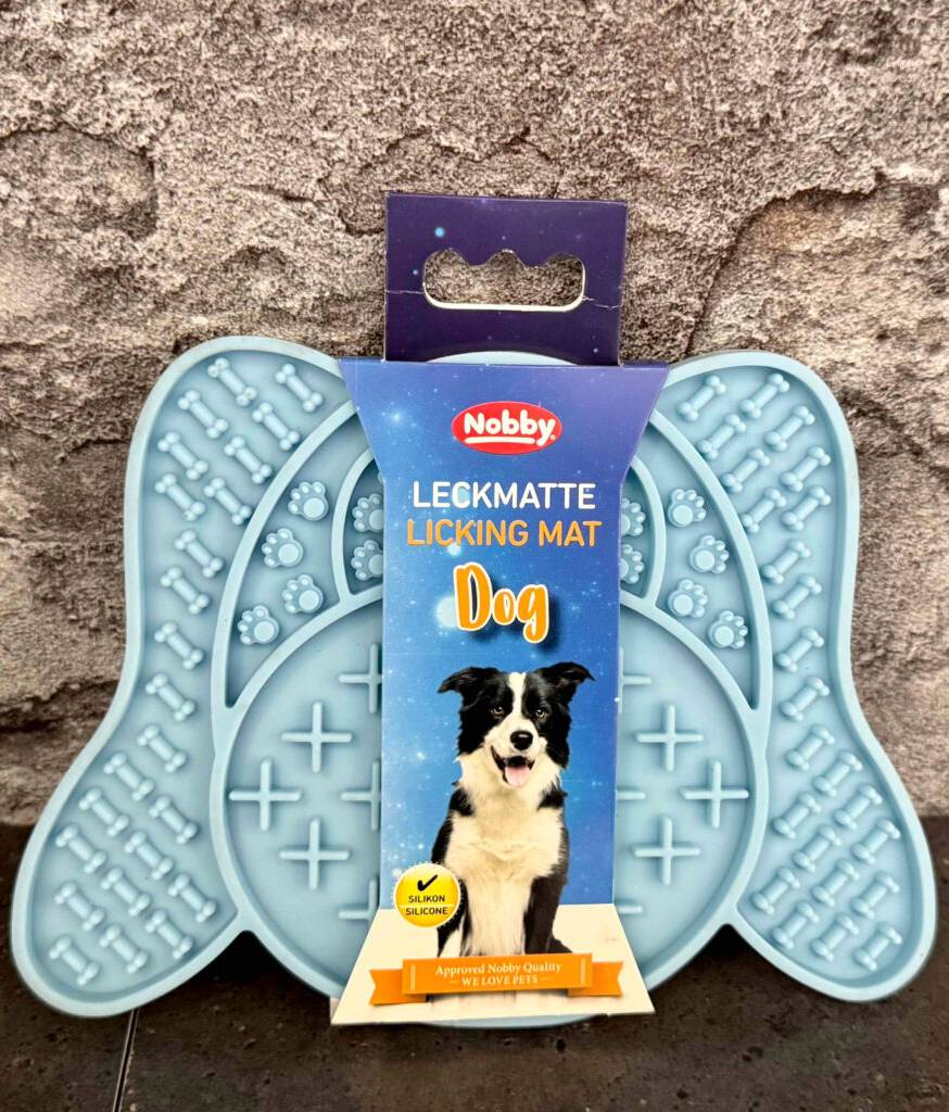Die hellblaue getestete Hunde-Leckmatte lehnt an einer Rauputzwand.