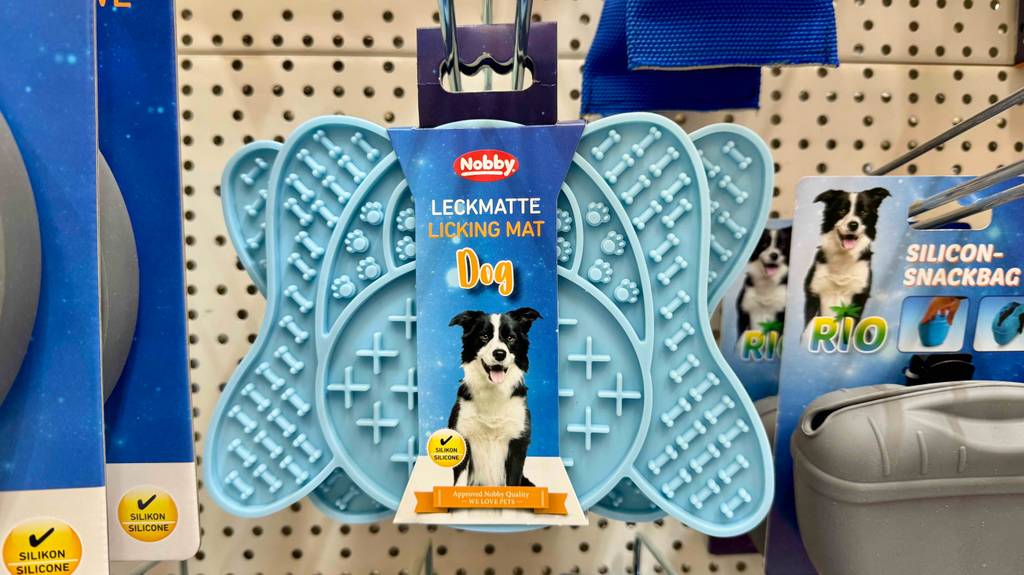 Im Test: Die Hunde-Leckmatte in Hellblau hängt an einem Verkaufsregal neben weiteren Utensilien für Hunde.