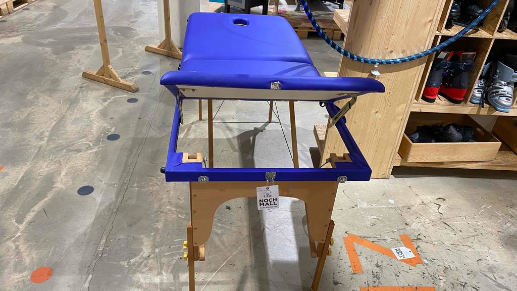 Ansicht auf eine blaue getestete Massageliege, dessen Kopfteil hochgestellt ist.