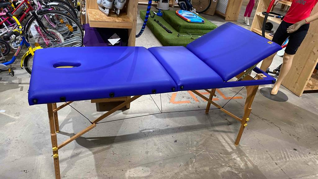 Eine blaue Massageliege im Test steht mit aufgeklapptem Holzgestell in einem Verkaufsbereich für Sportutensilien.