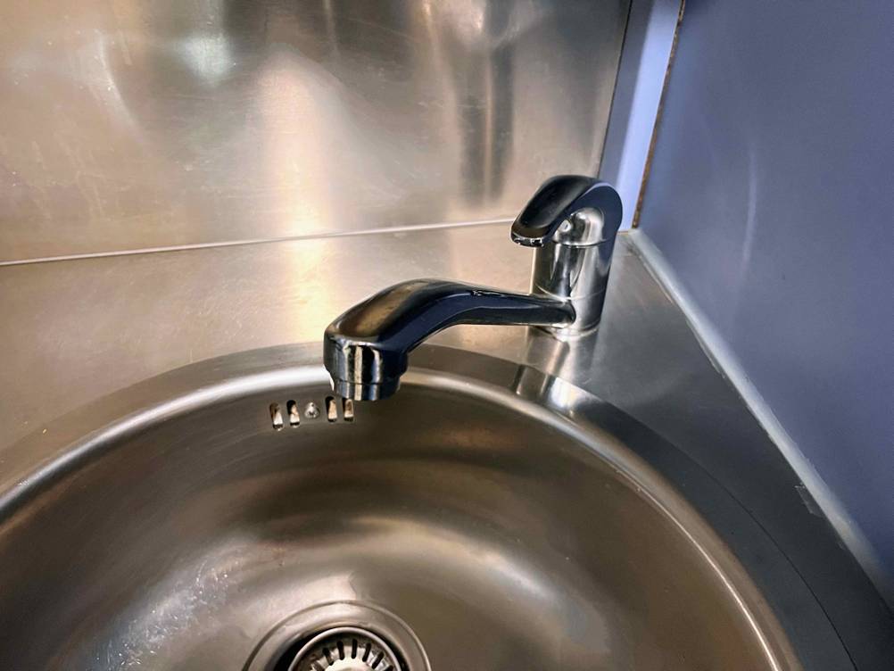 Nahaufnahme einer runden getesteten Küchenspüle aus Edelstahl inklusive Wasserhahn.