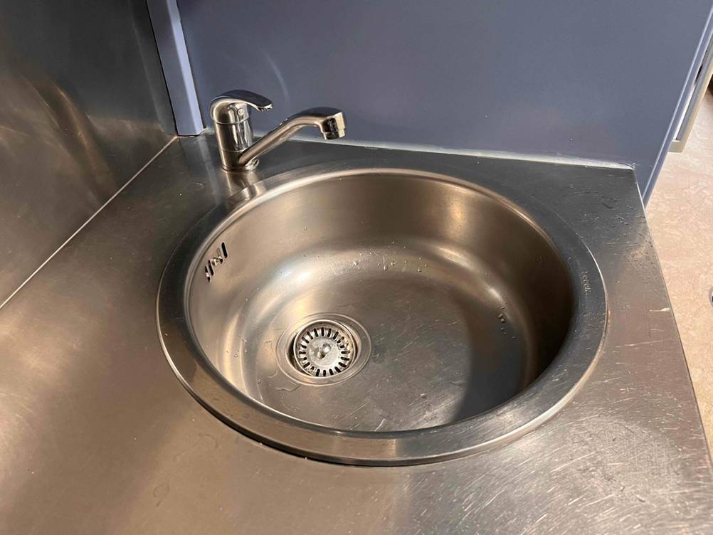 Gesamtansicht einer runden getesteten Küchenspüle aus Edelstahl inklusive Wasserhahn in Edelstahl-Arbeitsfläche.