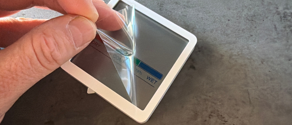 Eine Hand entfernt eine Schutzfolie vom Display vom Noklead-Hygrometer
