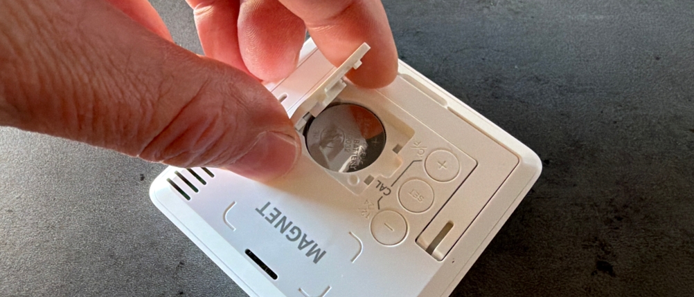 Eine Hand entfernt die Batterieabdeckung vom Noklead-Hygrometer