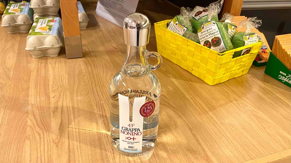 Eine Flasche des getesteten Grappas steht auf einem Tisch im Hintergrund mehrere andere Produkte.