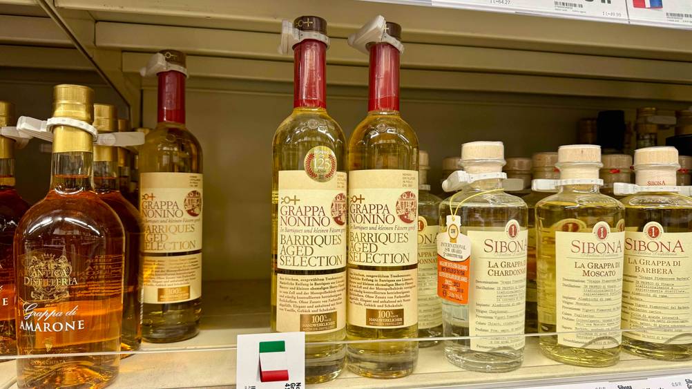 Mehrere Flaschen des getesteten Nonino-Grappas in einem Verkaufsregal neben anderen Produkten.