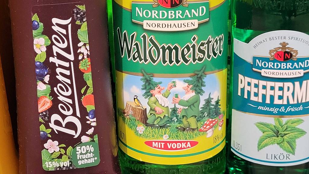 Auf dem Etikett von getestetem Waldmeisterlikör sind zwei Zwerge, die anstoßen.