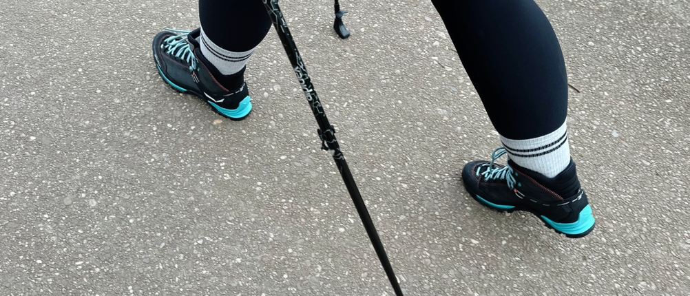 Eine Person geht mit Alpidex-Nordic-Walking-Stöcken auf Asphalt. Nur die Beine und die Stöcke sind im Bild zu sehen.