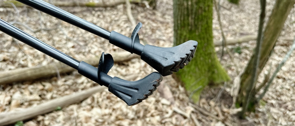 Zwei Alpidex-Nordic-Walking-Stöcke mit gummierten Aufsätzen sind im Wald zu sehen. Die Pads zeigen ein gezacktes Profil.
