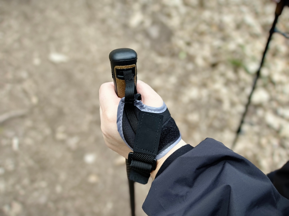 Eine Hand hält den Griff eines Gipfelsport Nordic-Walking-Stocks. Die Hand ist durch eine gepolsterte Schlaufe gesichert.