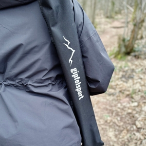 Eine Person trägt die schwarze Transporttasche von Gipfelsport im Wald. Das weiße Logo ist gut sichtbar.