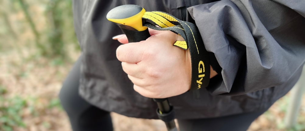 Eine Hand hält den Griff eines Glymnis-Walking-Stocks. Die Schlaufe ist schwarz-gelb und liegt eng am Handgelenk.