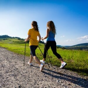 Zwei junge Frauen laufen mit Nordic-Walking-Stöcken.