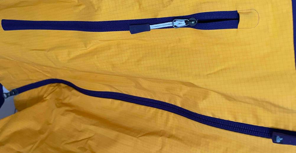 Detailansicht vom lila Reißverschluss einer gelben Unisex-Regenjacke im Test.