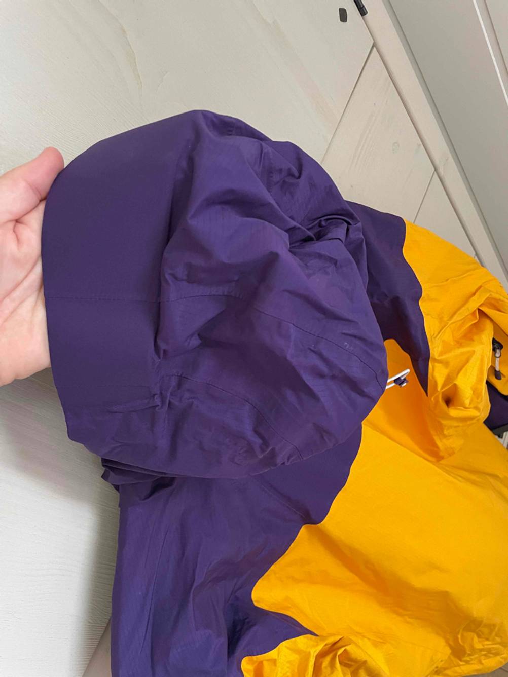 Regenjacke Unisex im Test: Eine Hand hält die lila Kapuze einer Jacke. 