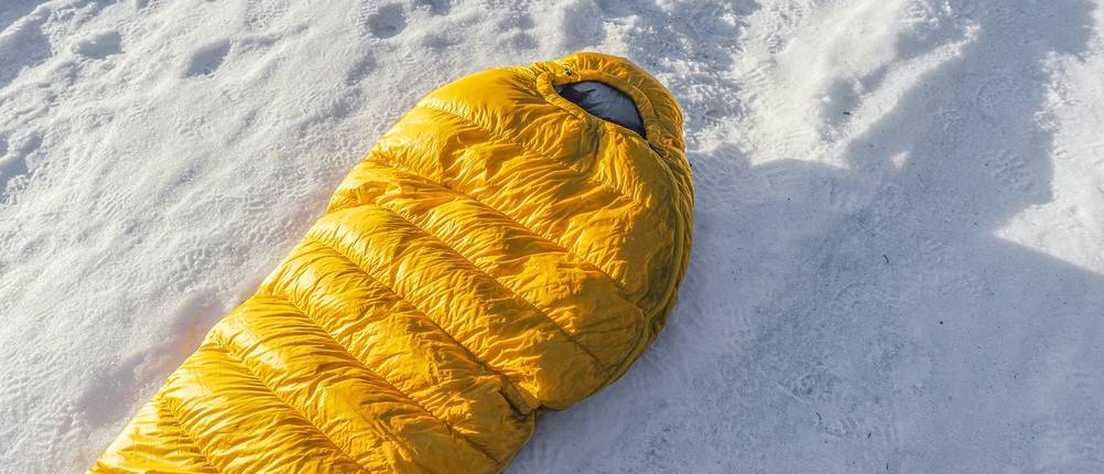 Getesteter gelber Schlafsack liegt auf einem verschneiten Untergrund.