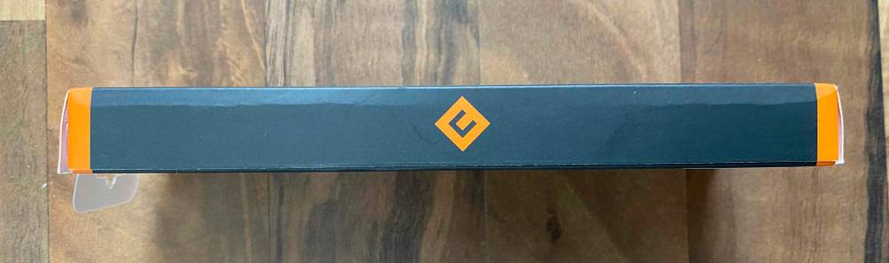 Ansicht einer langen, schmalen Seite der grün-orangen Verpackung vor Holzhintergrund von einem USB-C-Hub im Test.
