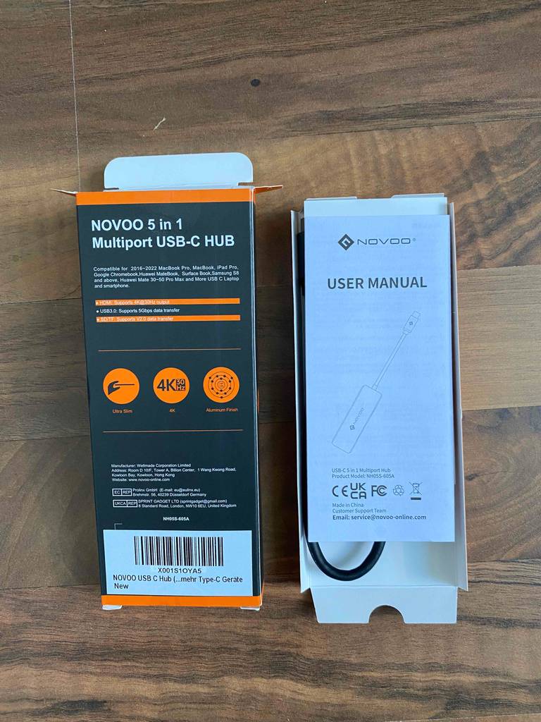 USB-C-Hub im Test: Das Modell von Novoo 5 in 1 befindet sich unter seinem User-Manual neben der Originalverpackung auf einem Holzboden.