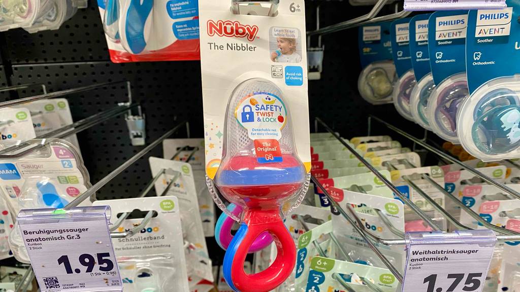 Fruchtsauger-Test: Ein rot-blauer Nuby The Nibbler hängt in seiner transparenten Verpackung an einem Verkaufsregal mit anderen Baby-Saugern.