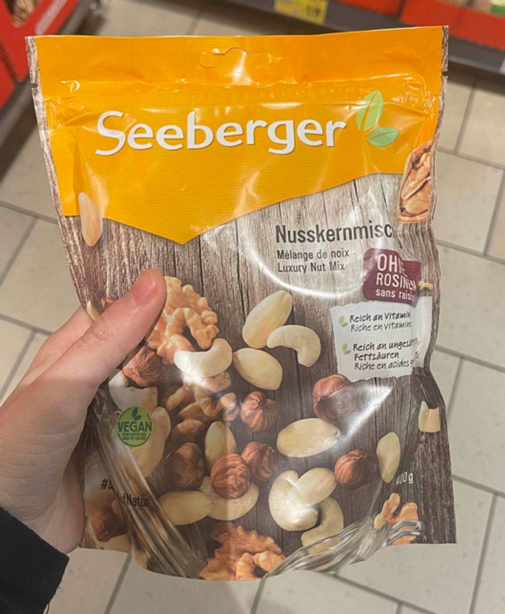 Eine Hand hält die wiederverschließbare Tüte von Seeberger, in der sich die Nussmischung im Test befindet, über einem weißen Fliesenboden.