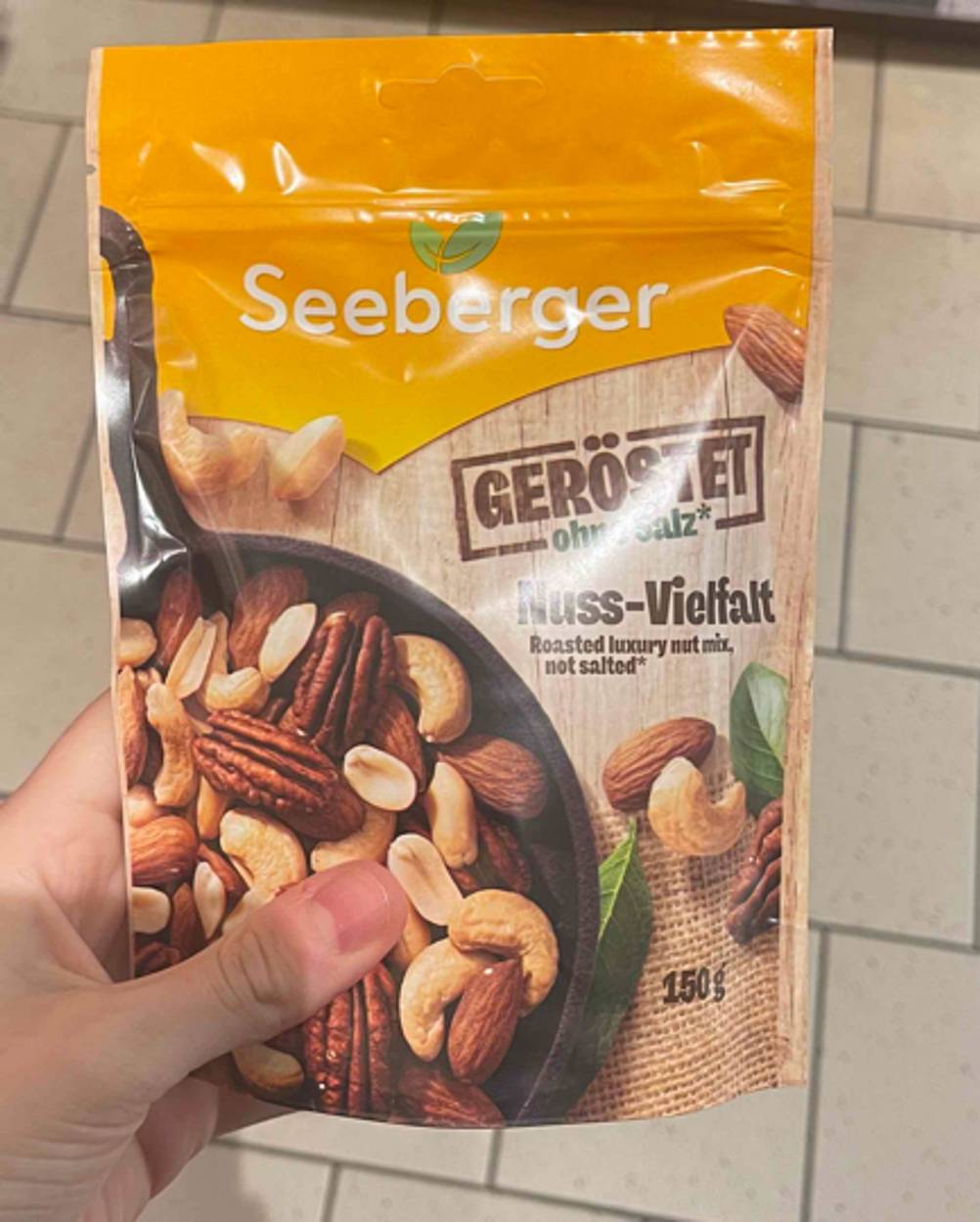 Die getestete Nussmischung der Firma Seeberger in der wiederverschließbaren 150-g-Tüte im gelben Design wird in einer Hand gehalten.