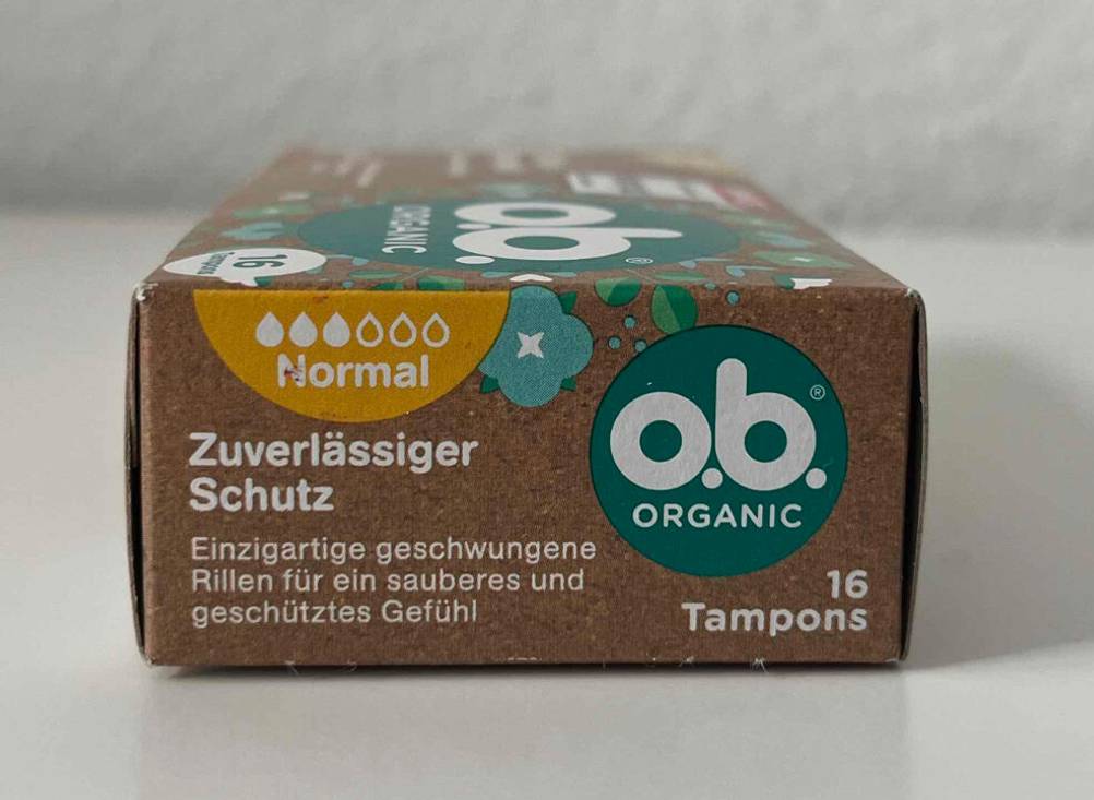 Getestete Bio-Tampons mit normaler Saugkraft befinden sich in einer braunen Schachtel von o.b., die auf einer weißen Fläche steht.