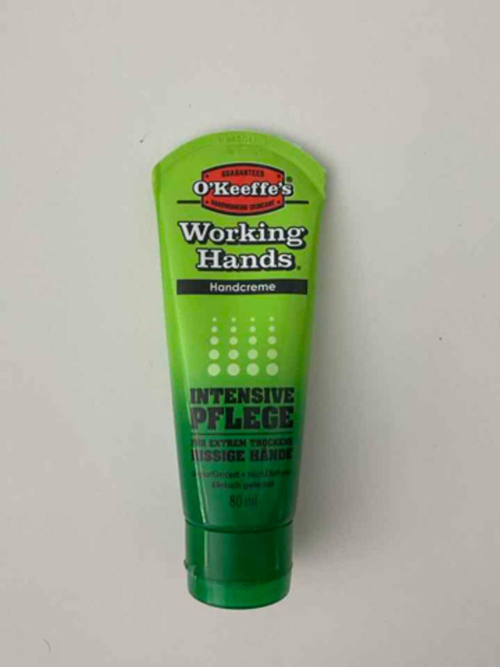 Hautschutzcreme im Test: Eine grüne Tube mit dem Markenzeichen O’Keefe’s Working Hands liegt auf einem weißen Untergrund.