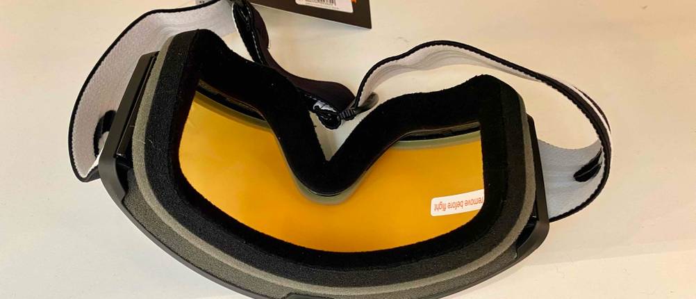 Skibrillen im Test: Ansicht der schwarzen Schaumstoff-Gesichtsauflage einer Skibrille im Test inklusive orangefarbener Sichtscheibe und schwarz-weißem Kopfband auf heller Fläche
